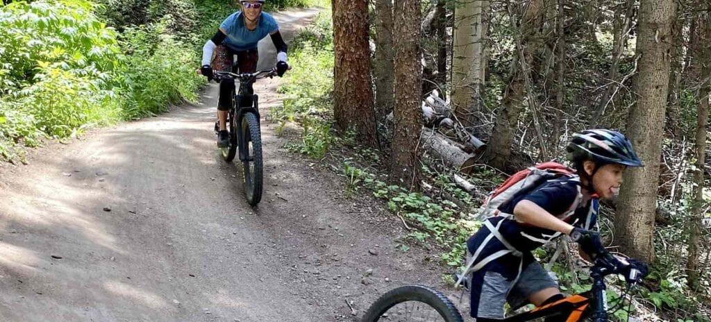 Smiling woman and child mountain biking through Telluride forest.