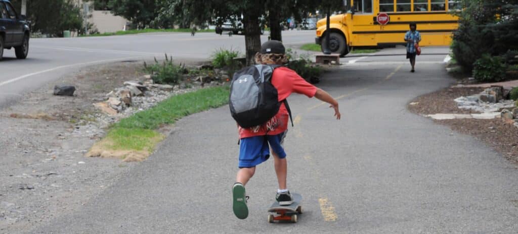 Student with backpack skateboards to schoolbus in summer.