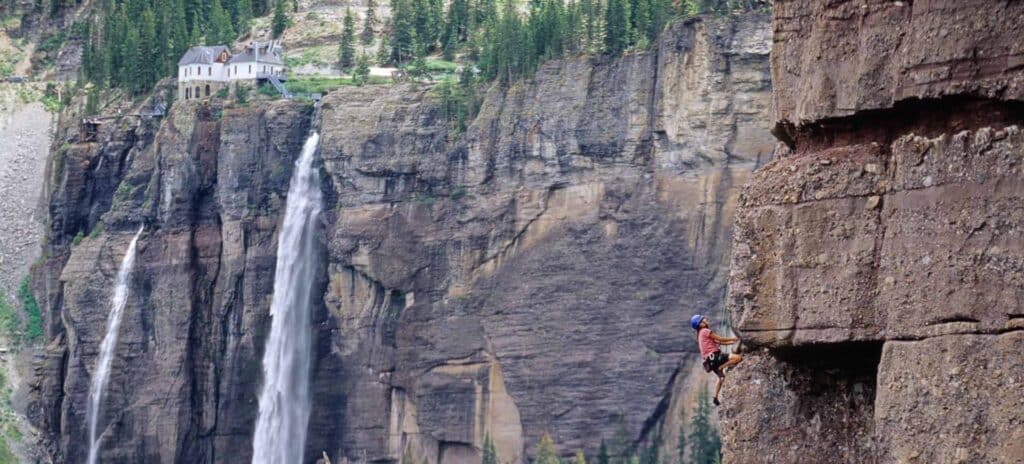 Rock climber with a Telluride waterfall and hydro electric power station in the background.
