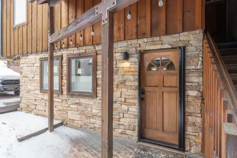 545 West Pacific ground floor condo winter exterior stone wall and lighted, wooden, windowed entry door. A Telluride real estate rarity.