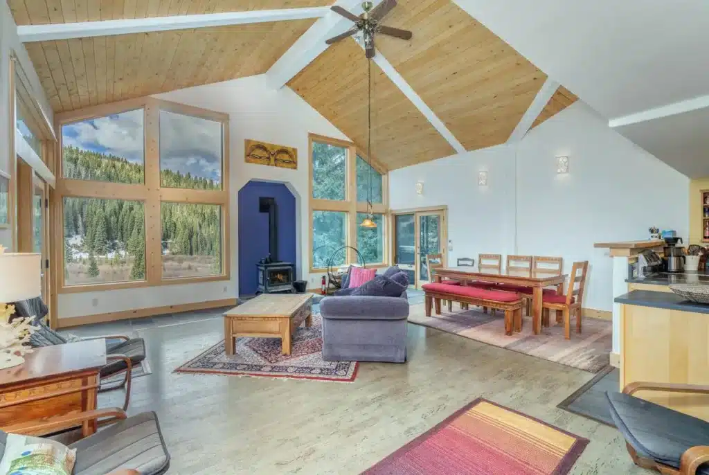 Interior view of real estate listing 135 Marmot Way Ophir (Trout Lake), with airy living space, wood stove and forested, mountain views.