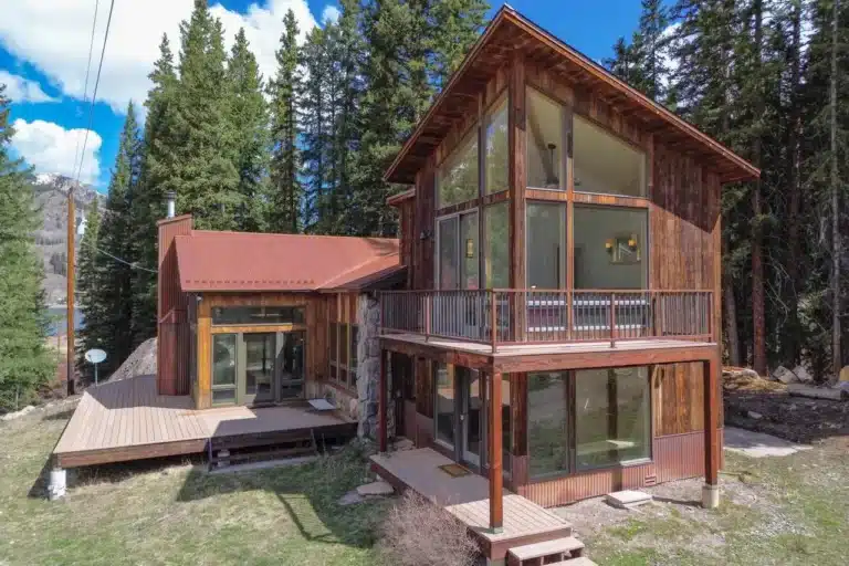 Sunny, exterior view of real estate listing 135 Marmot Way Ophir (Trout Lake), with decks, forest and blue skies