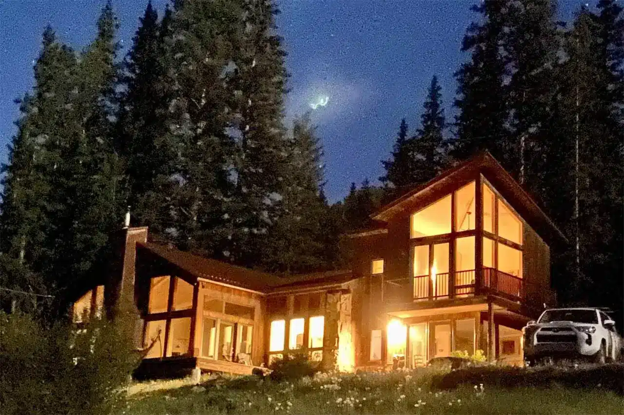 Starry night illuminated exterior view of real estate listing 135 Marmot Way Ophir (Trout Lake), with forest in the background.
