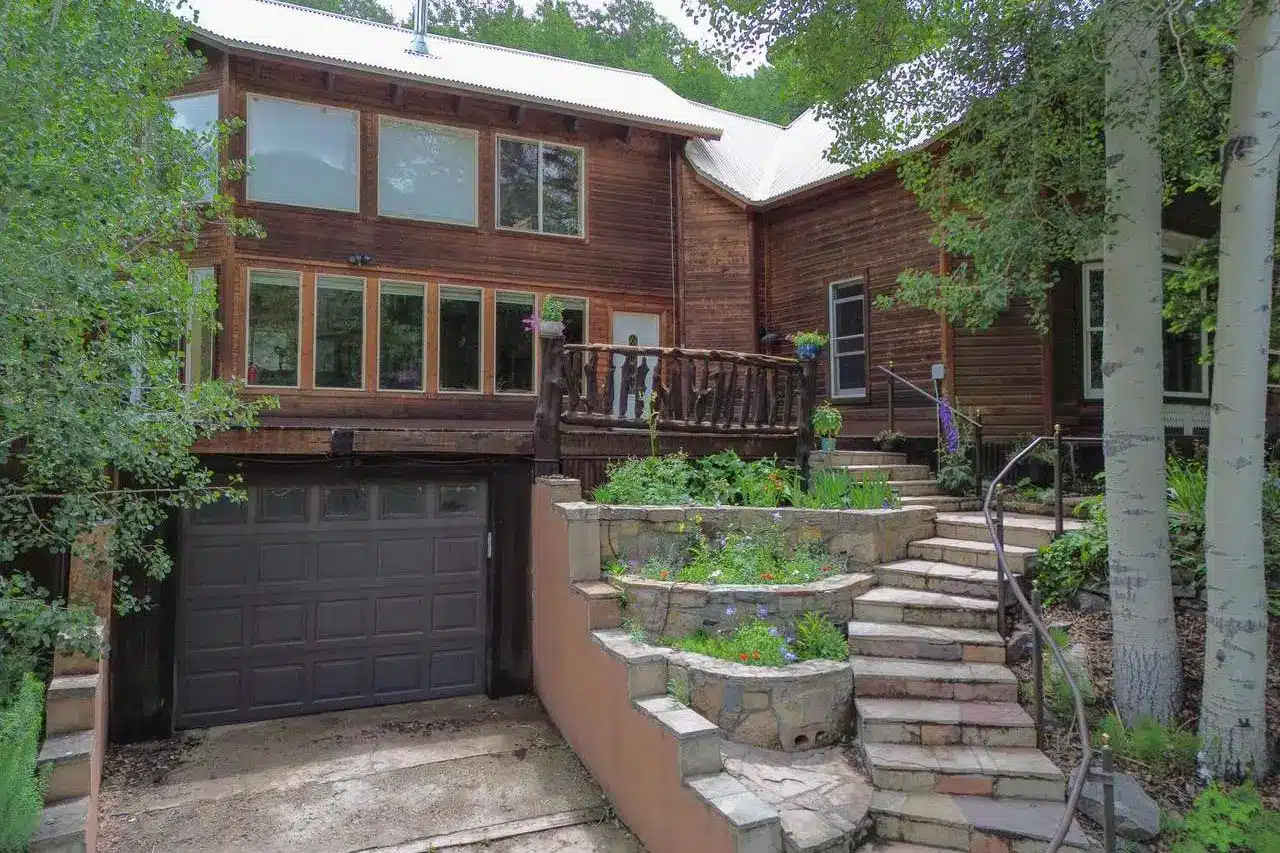 Summer wooded exterior of real estate listing 301 E Mantz Ave., Rico, Colorado. With curving stone stairs, planters and decks.