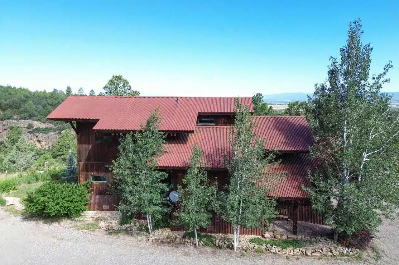 Summer exterior of real estate listing 423 Beaver Pines Rd, Norwood, with metal roofs ans surrounding trees.