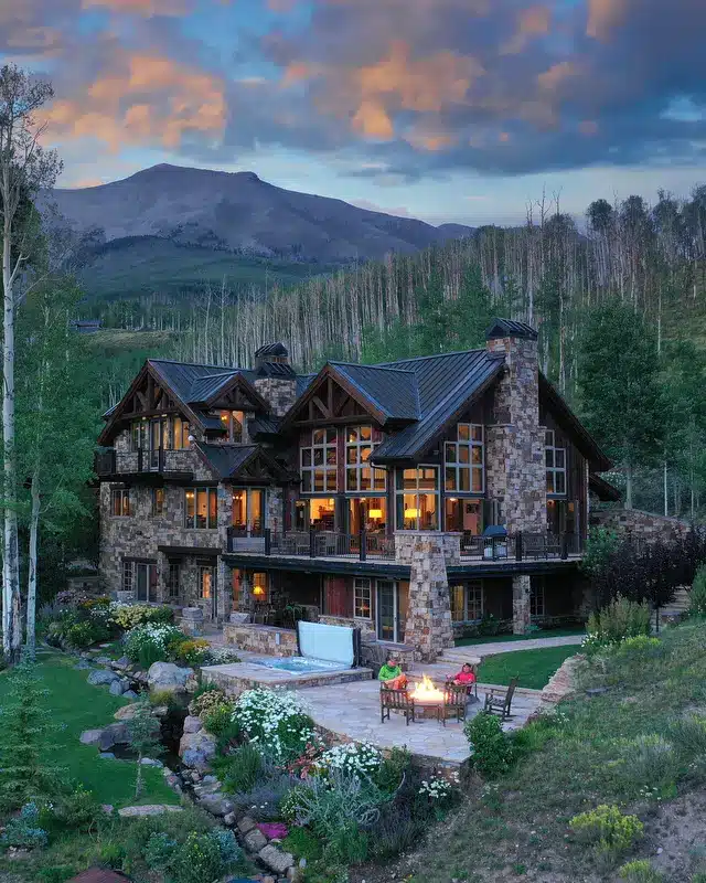 Telluride area home illuminated at dusk with alpine forest and mountains in background.