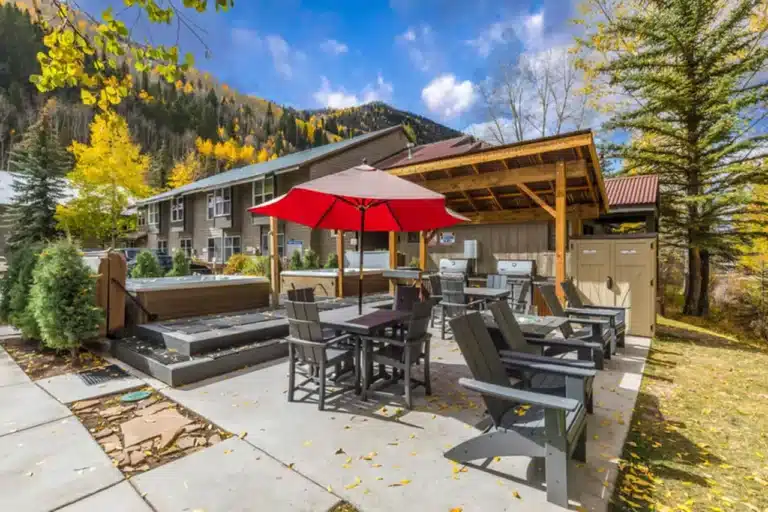 Sunny, autumn, exterior patio area of Mountainside Inn Telluride condo real estate listing with seating and umbrella.