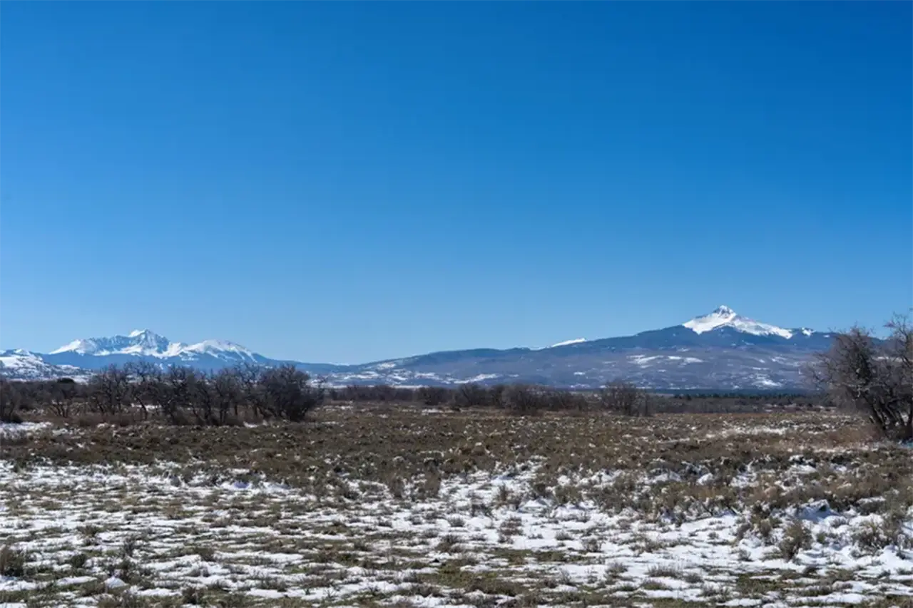Blue sky view of Shimkonis Partners real estate listing, 192 S Avalon Dr, Norwood, snow dusted expanse of land and snow capped peaks beyond.