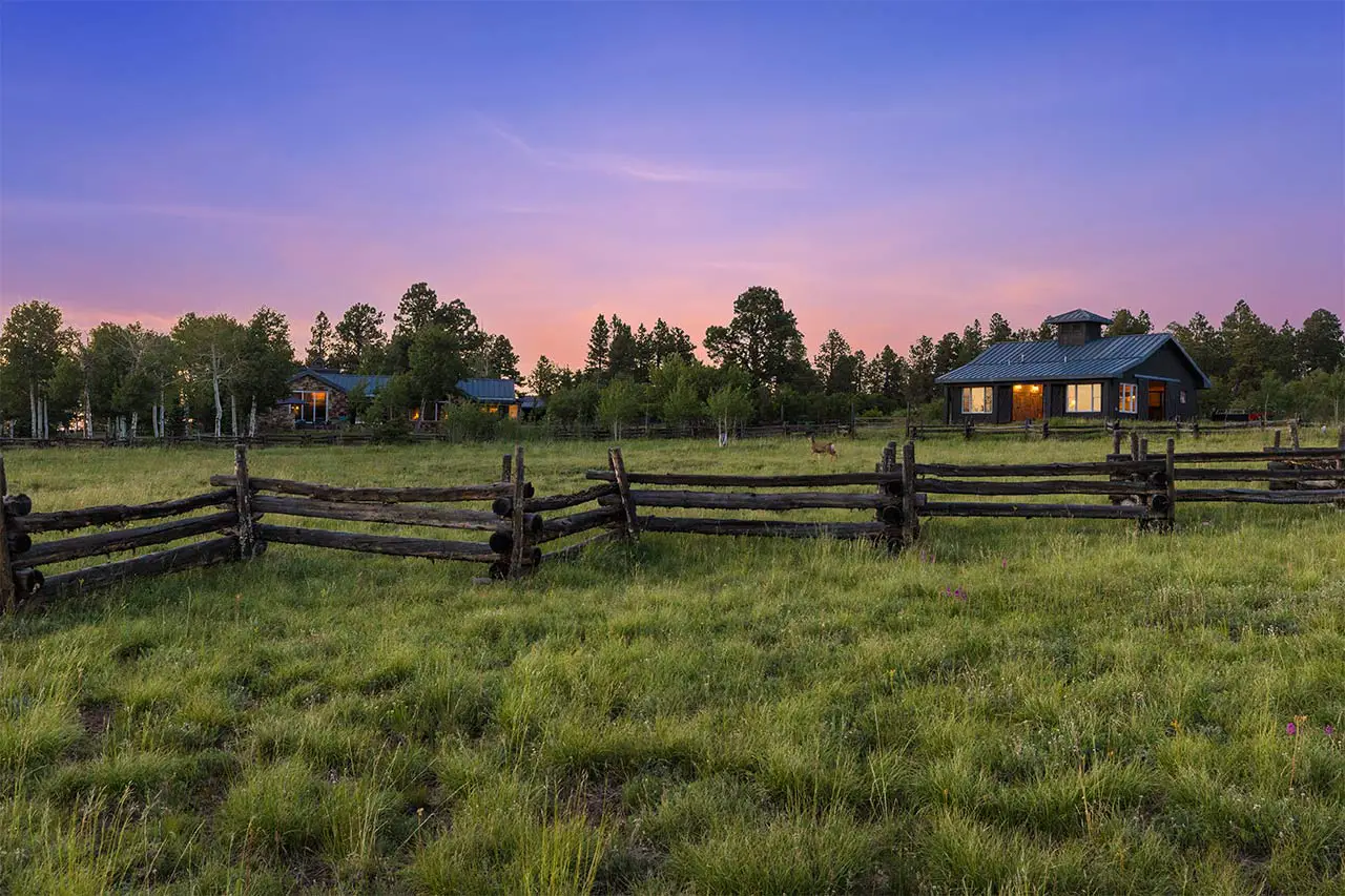 Shimkonis Partners Telluride area real estate listing, Laughing Dog Ranch: illuminated main house and barn at dusk with fence, summer lawn and aspens