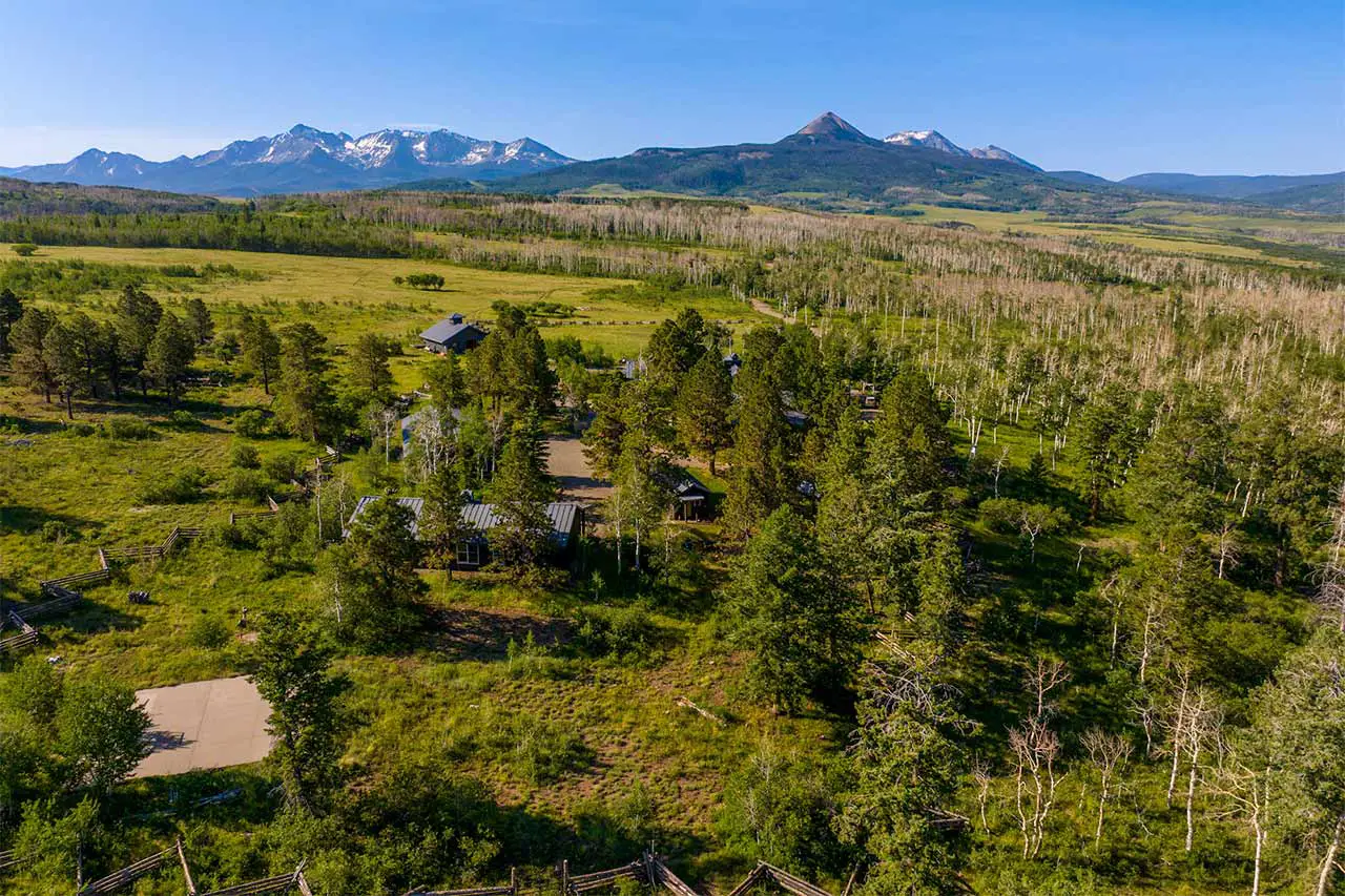 Shimkonis Partners Telluride area real estate listing, Laughing Dog Ranch: a rare 243-acre sanctuary, summer blue-sky aerial view withproperty buildings and mountains