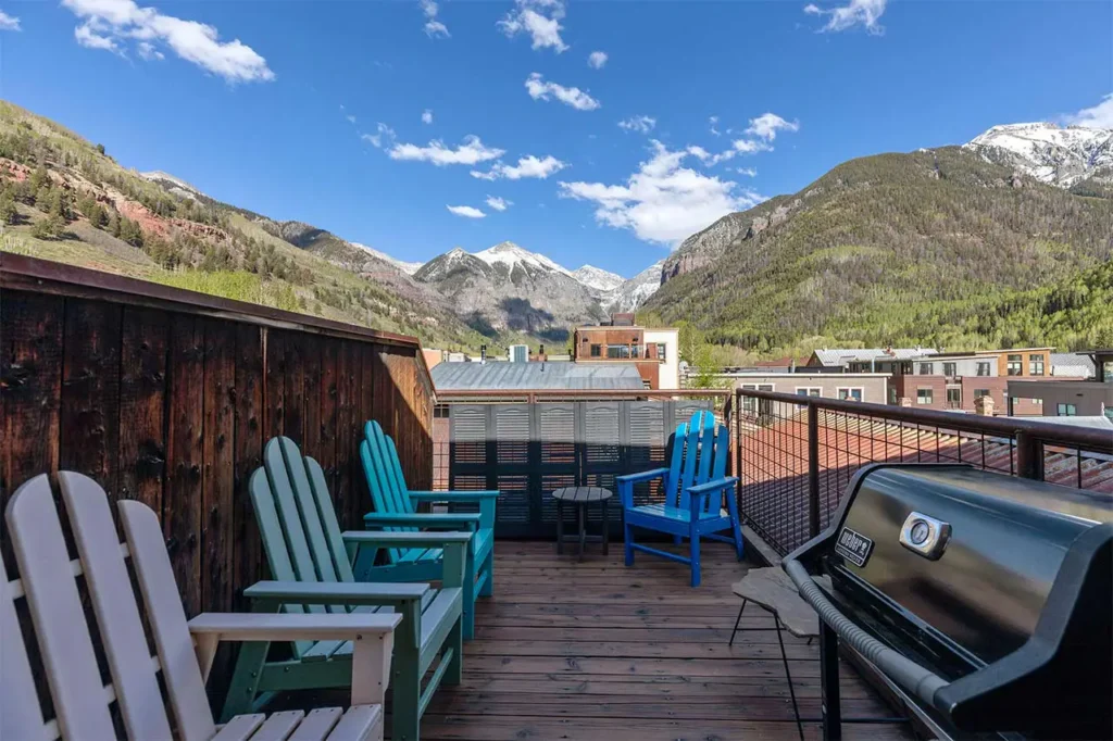 Shimkonis Partners real estate listing, 110 S Pine St, Telluride, sunny rooftop deck with multicolored adirondack chairs and verdant mountains beyond