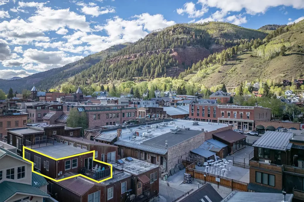 Shimkonis Partners real estate listing, 110 S Pine St, Telluride, sunny aerial building exterior with penthouse unit outlined and verdant mountains beyond