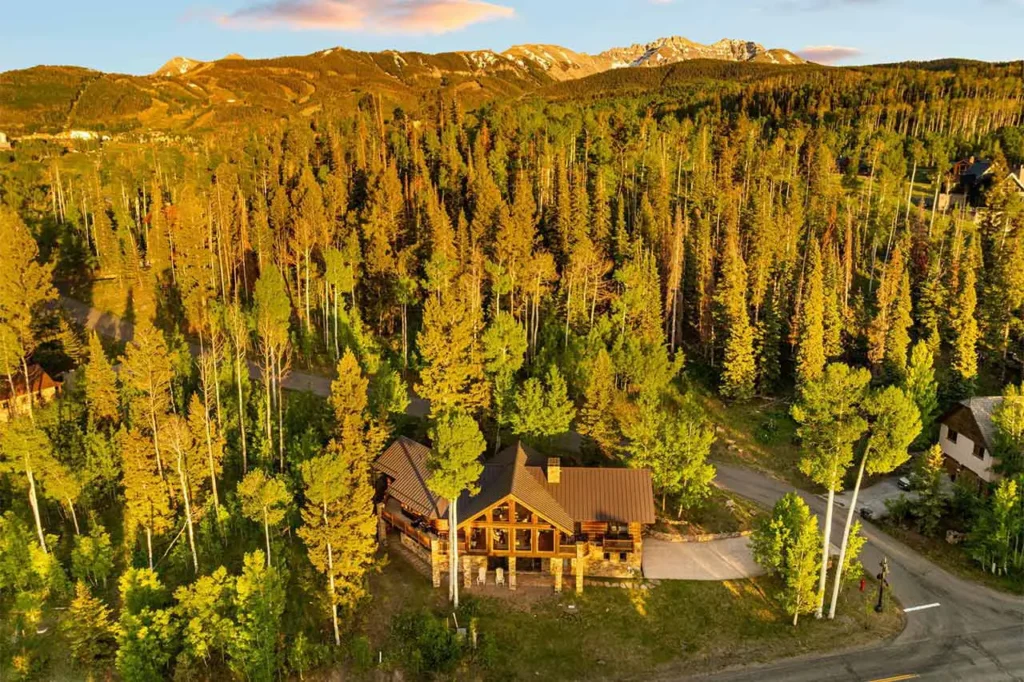 Sunny aerial view of Shimkonis Partners Telluride area real estate listing, 103 Birdie Drive, Mountain Village, featuring surrounding forest and distant peaks