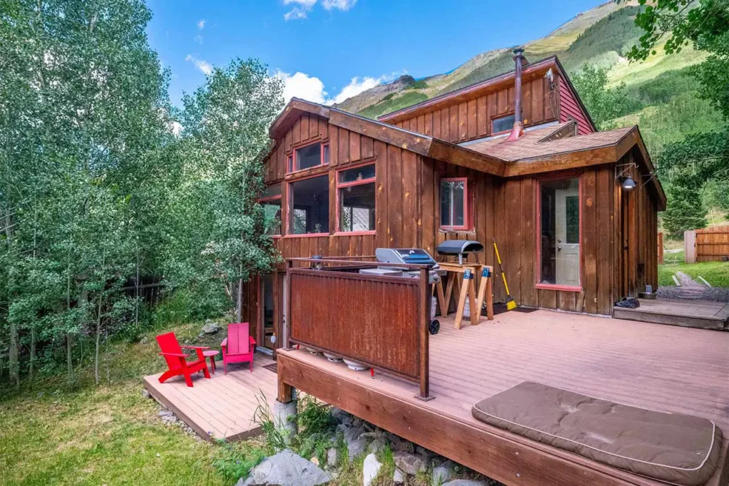 Sunny exterior view of Shimkonis Partners Telluride area real estate listing, 30 Aurum Street, Ophir, with deck, adirondack chairs and yard