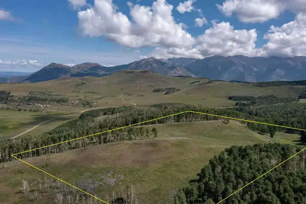 Aerial summer view of Shimkonis Partners Telluride real estate listing, TBD East Wilson Mesa 60M, Placerville, featuring a large parcel of land surrounded by forest with mountain views and property outline
