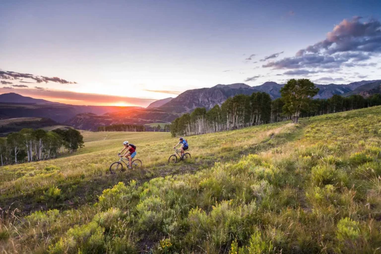 Telluride summer mtb sunset Two mountain bikers crossing a Telluride mesa with a scenic sunset illuminating the mountains