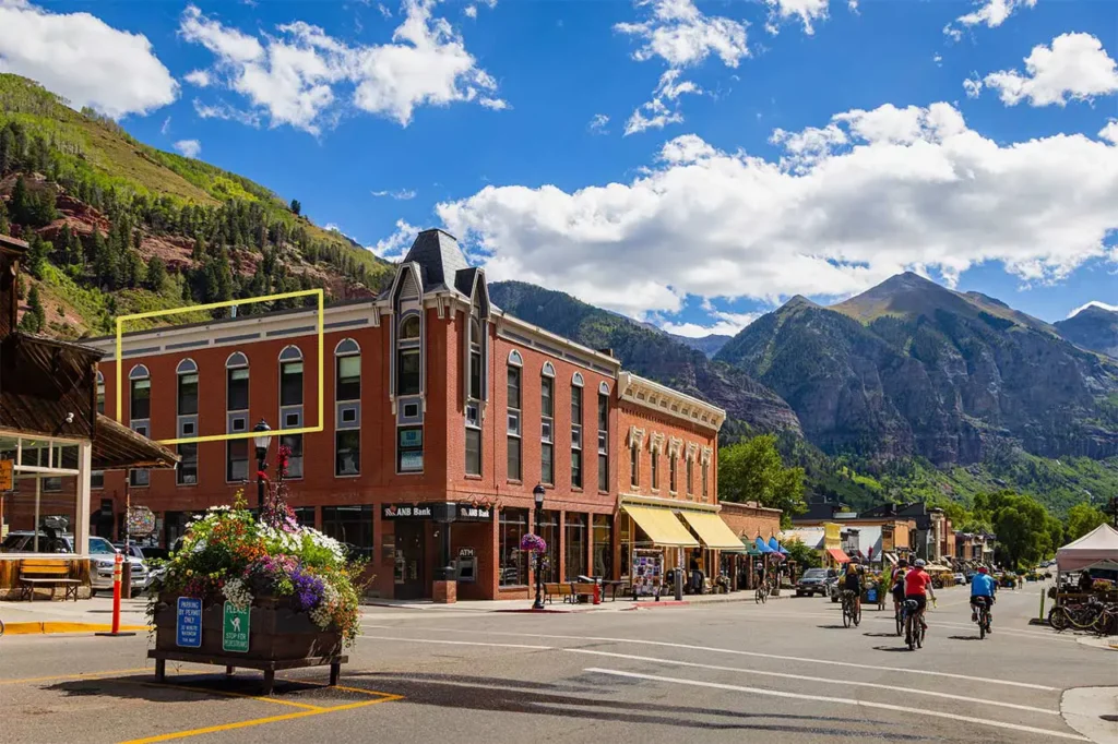 Summer exterior of Shimkonis Partners Telluride real estate listing, Black Bear #302, with town and mountain views and outline of 3rd floor condo windows